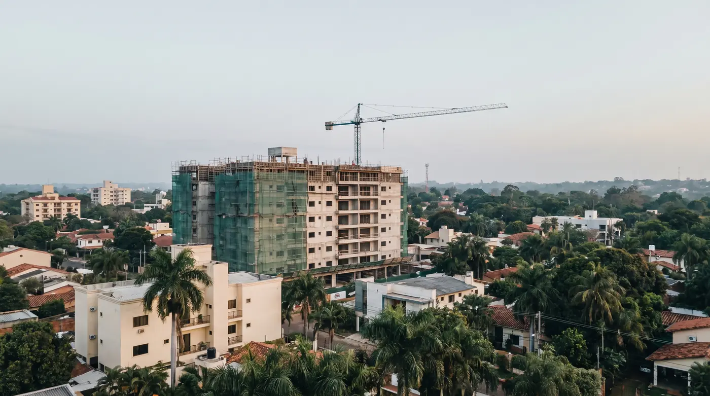 Immeuble résidentiel en construction avec une grue à Asunción, entouré de maisons basses et de palmiers